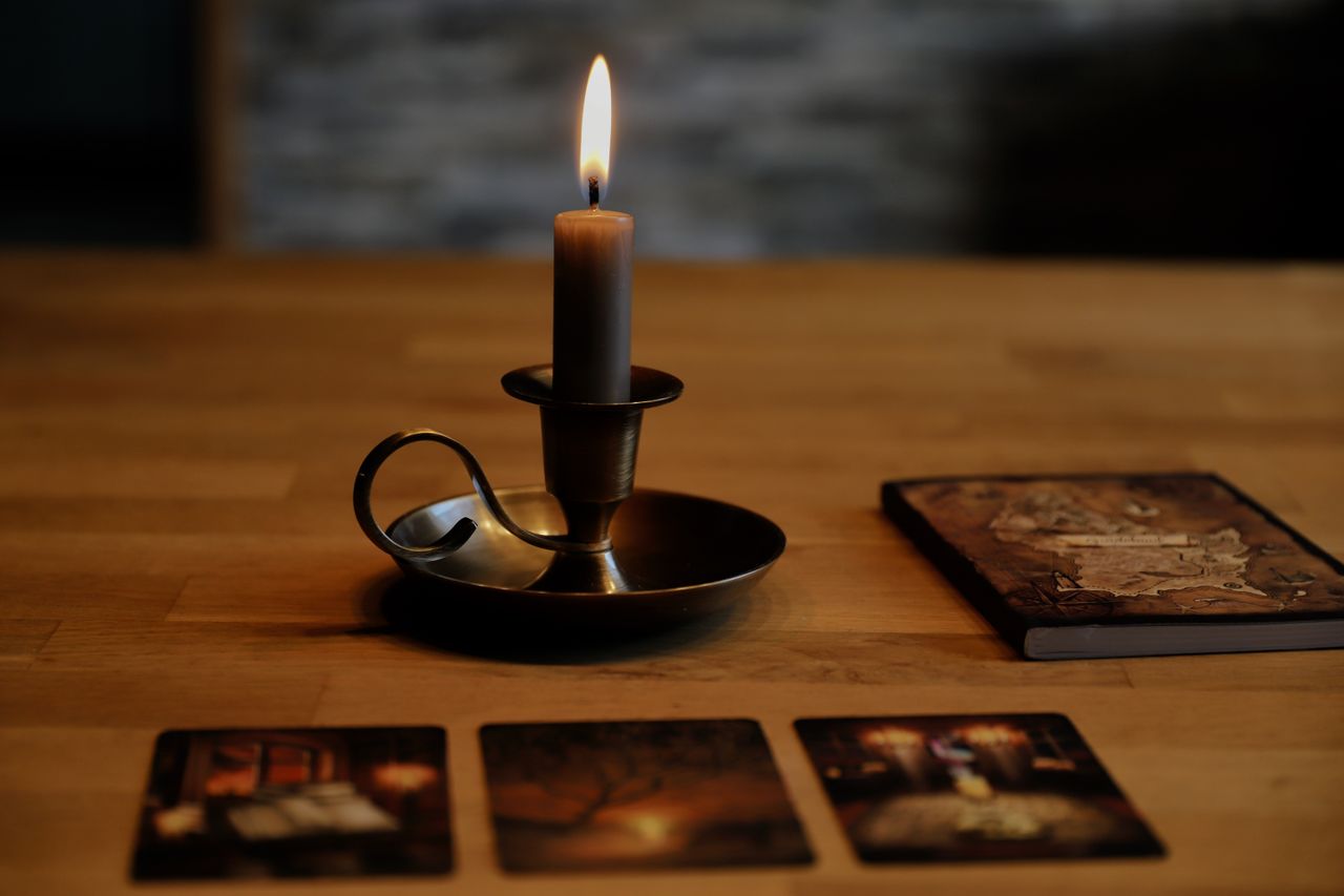 Moody setup with candleholder, tarot cards, and aged book on wooden table.