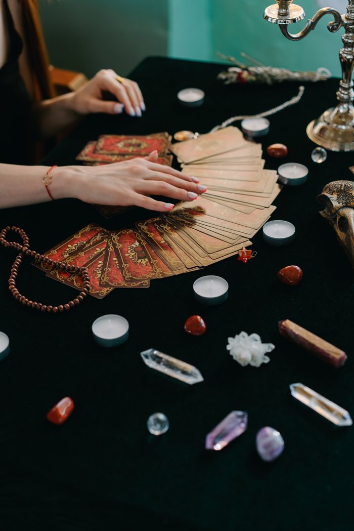 About High angle of crop anonymous female fortune teller with tarot cards and stones with candles during divination process
